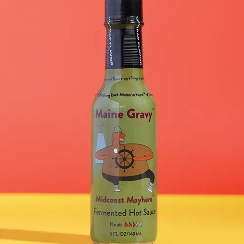 Maine Gravy Midcoast Mayhem hot sauce bottle on a colored background