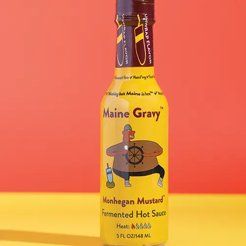 Maine Gravy Monhegan Mustard hot sauce bottle on a colored background