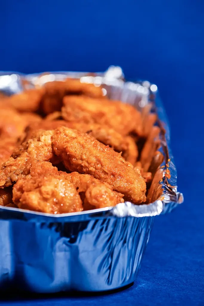 Chicken wings tossed with hot sauce in an aluminum pan