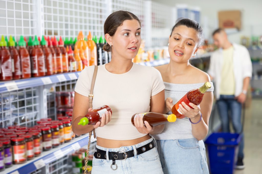 Two women comparing sauces in market